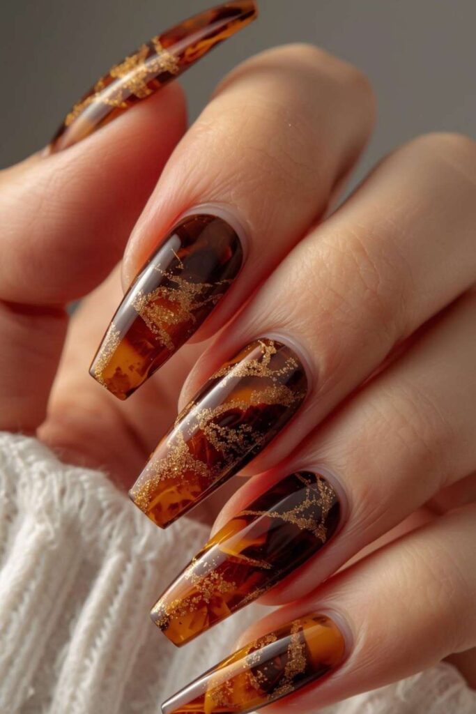 Amber and brown tortoiseshell acrylic nails with glossy marble-like patterns and luxury manicure styling.