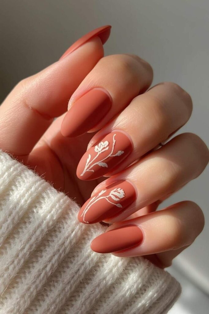 Matte terracotta oval acrylic nails with delicate botanical line art creating an earthy Trendy Acrylic Nails 2026 manicure.