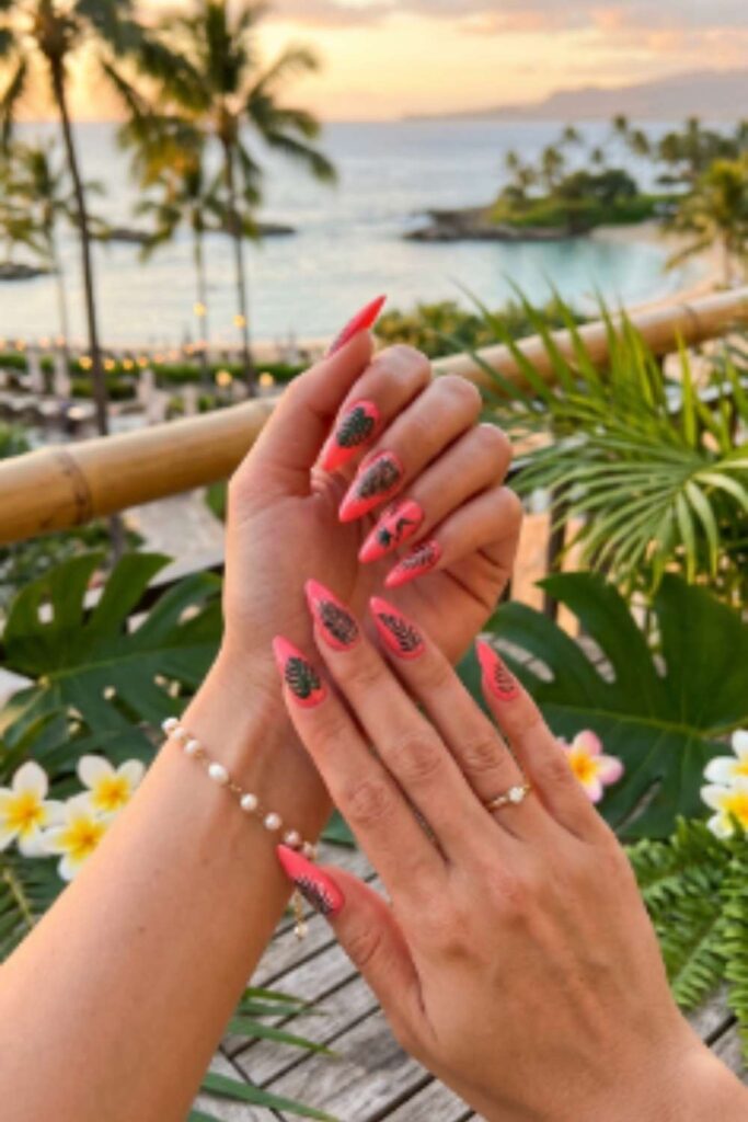 Coral pink stiletto nails featuring tropical palm leaf nail art with glossy gel finish for a vibrant vacation-ready manicure.