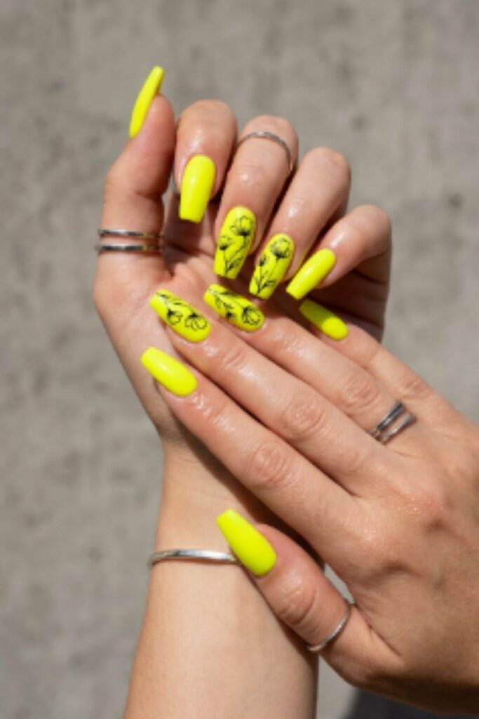 Neon yellow long nails featuring minimalist black floral outlines and glossy gel finish for a bold modern manicure.
