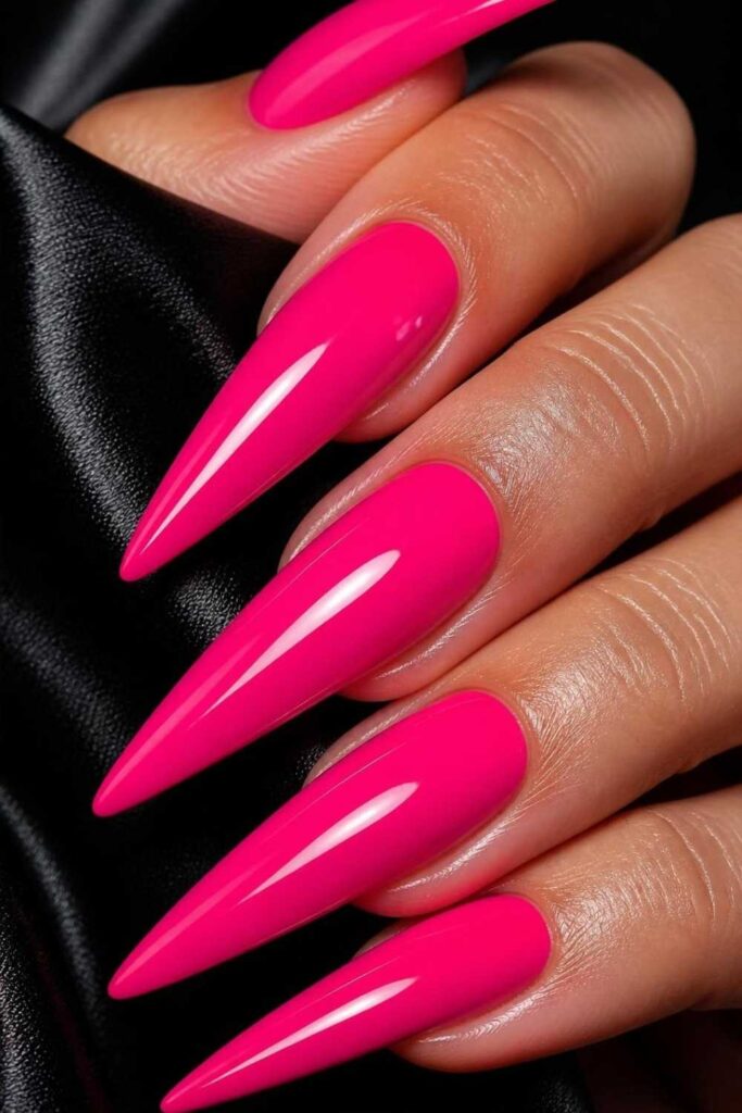 Long hot pink stiletto acrylic nails with an ultra-glossy finish creating a bold and glamorous manicure.