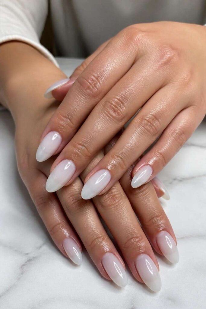 Long almond nails with translucent milky white gel polish and glossy finish creating a clean spring manicure.