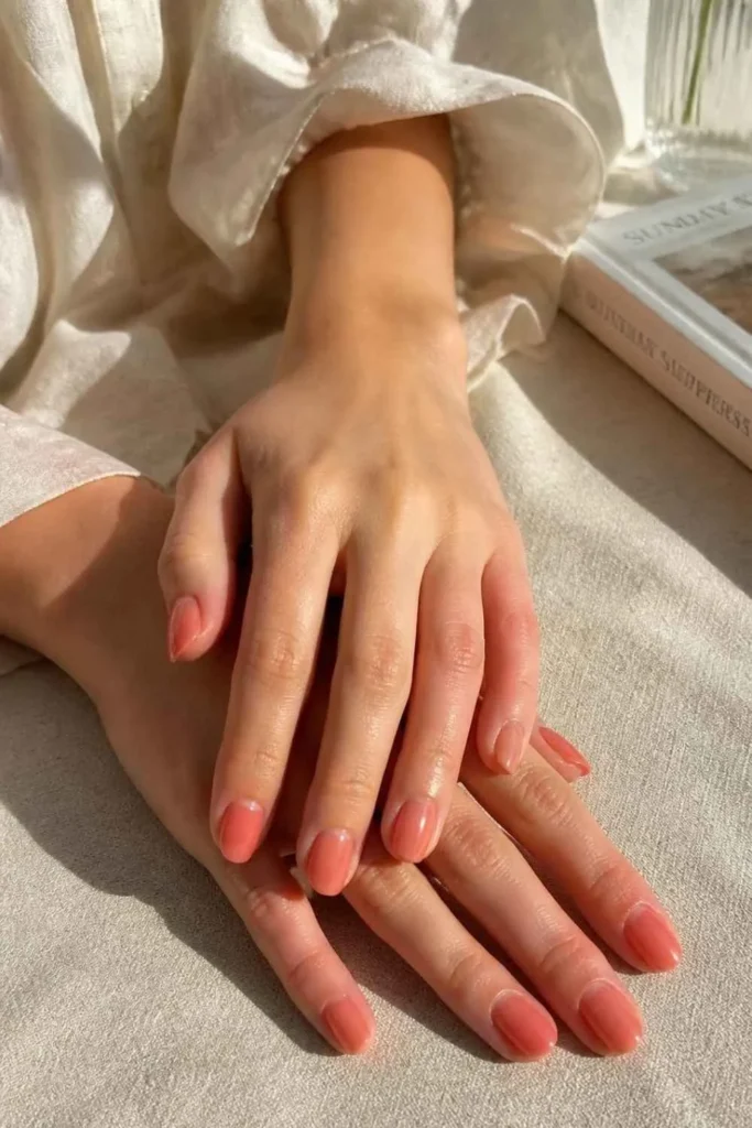 Sheer coral jelly short professional nails with rounded edges and translucent glossy finish on natural healthy nails.