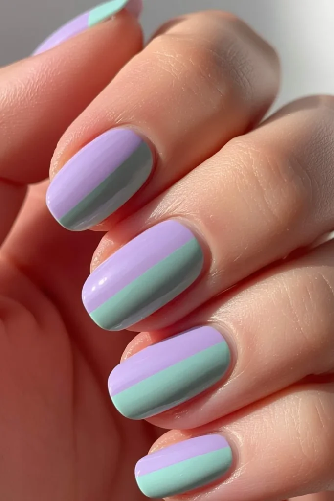 Short rounded nails with alternating lavender and mint pastel polish in a glossy two-toned manicure creating a fresh spring-inspired colorful nail design.