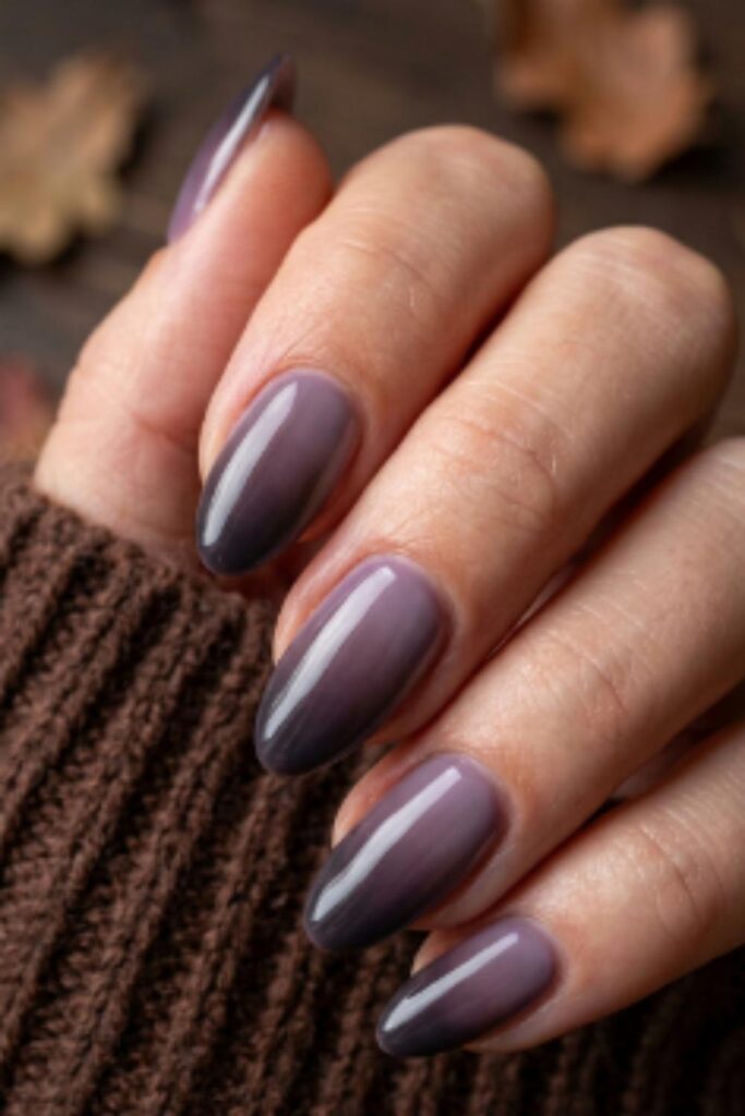 Close-up of smoked plum almond nails with soft blurred shadow edges and glossy finish creating a moody dark romantic fall nail design.