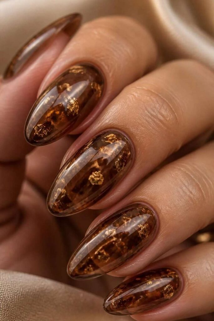Translucent mocha brown jelly acrylic nails with delicate gold foil flecks creating a glossy stained-glass manicure effect.