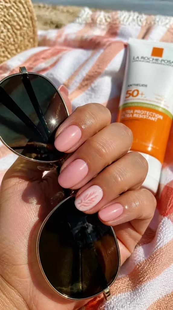 Glossy summer gel manicure holding sunglasses beside beach accessories under warm sunlight.